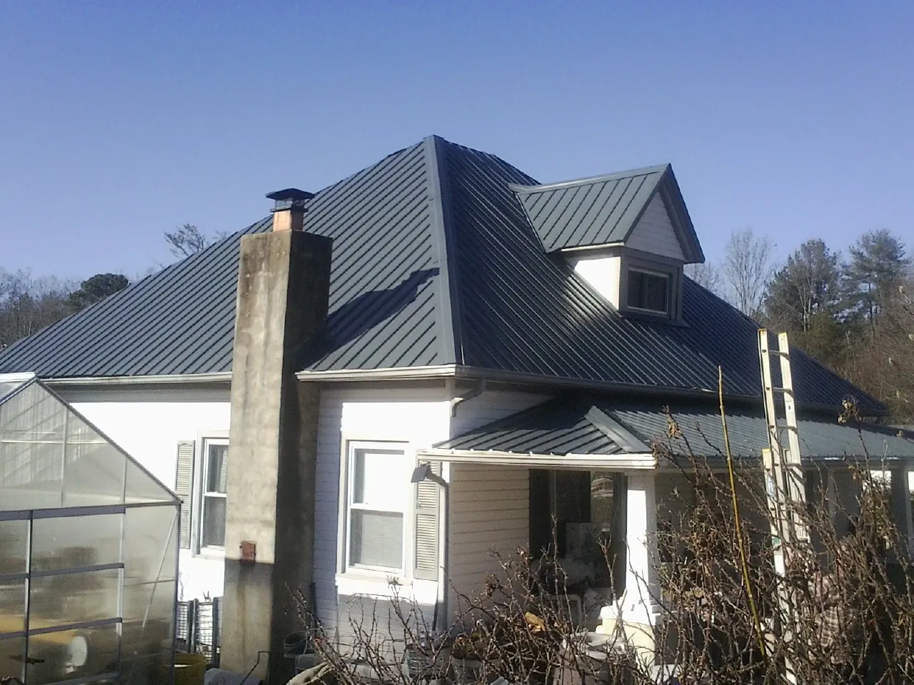 Dark blue standing seam metal roof on a white farmhouse with dormer — Slate & Tile Roof Repair by Roofing Brothers in Lusk