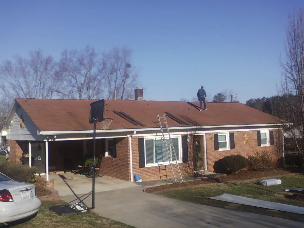Roofer stripping a shingle roof on a brick ranch before metal panels in Lusk