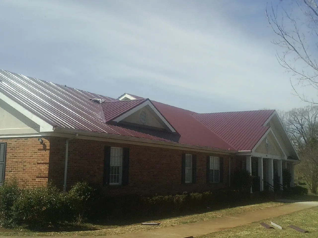 Red metal roof with gabled entries on a long brick building, from a Hail Damage Roof Repair job in Lusk