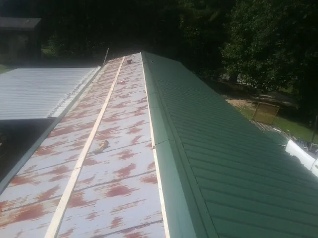 Old rusted panels beside newly installed green metal roofing — Wind Damage Roof Repair by Roofing Brothers in Lusk