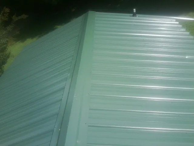 New green metal panels meeting at the ridge of a roof — Flat Roof Repair work by our crew in Lusk