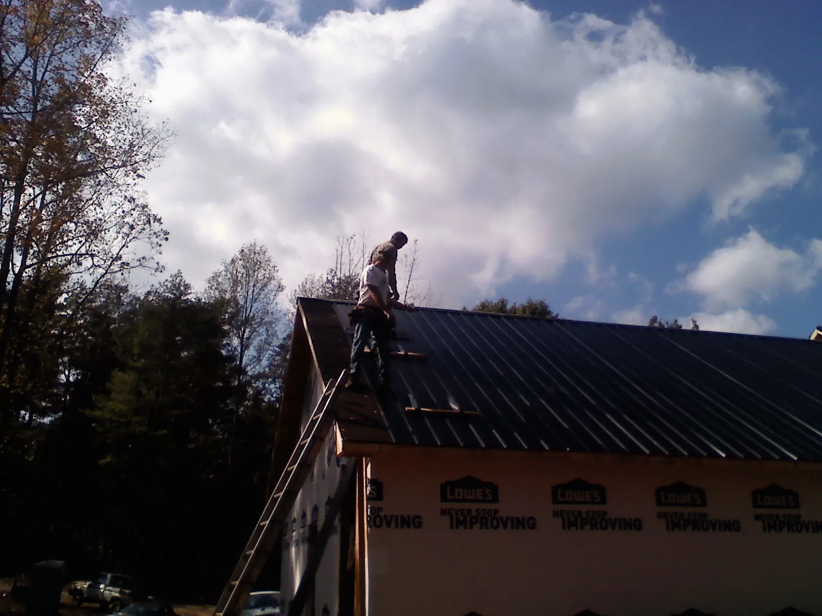 Roofer fastening dark metal panels high against a cloudy sky, from a Roof Inspection job in Lusk