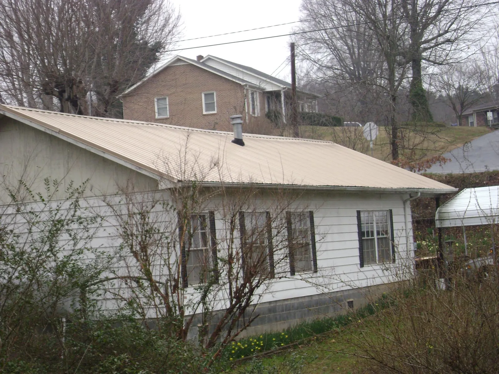 Tan metal roof on a white sided house set into a hillside — Commercial Roofing by Roofing Brothers in Lusk