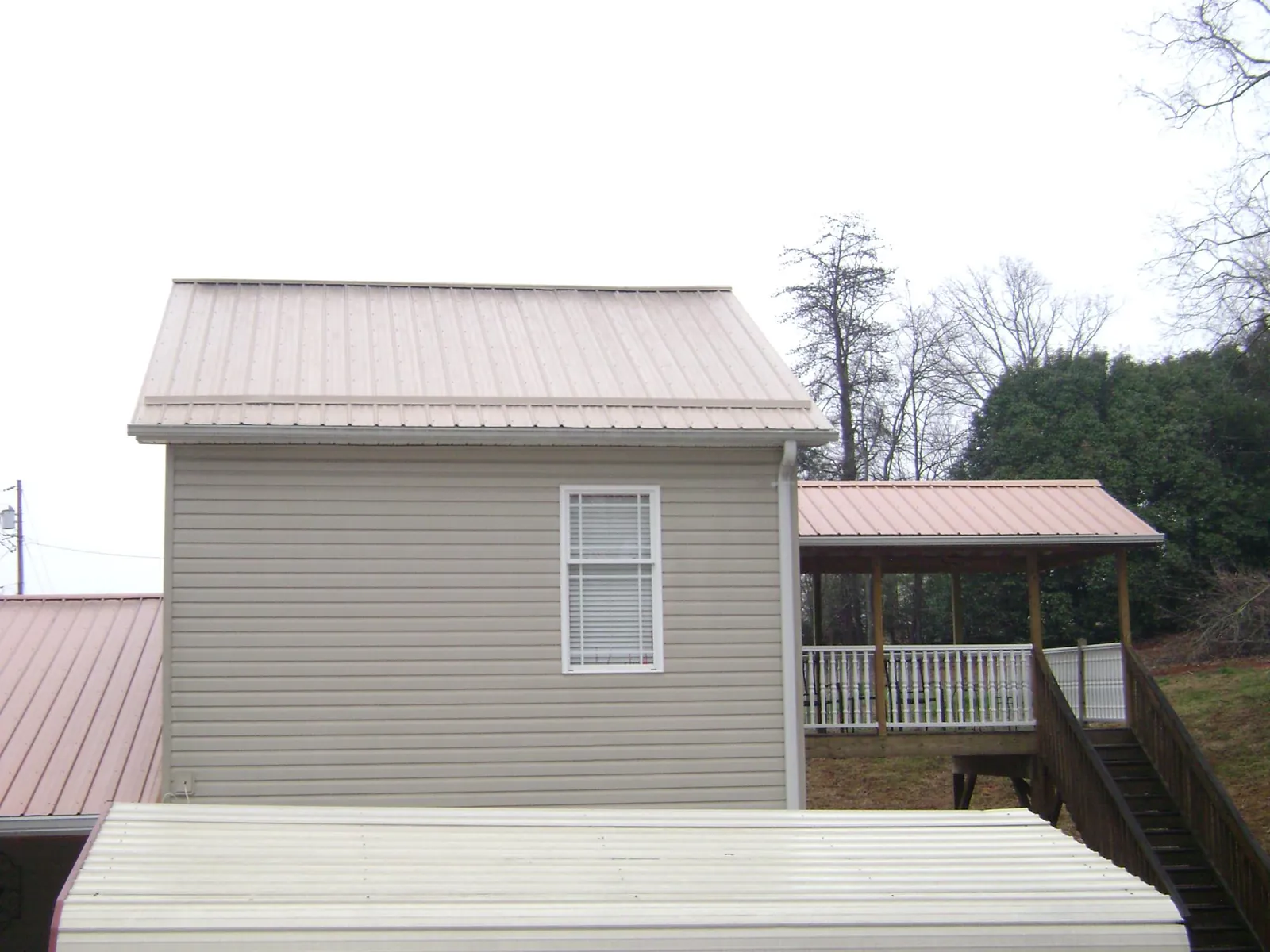 Tan metal roofs on a two story addition and attached porch, from a Roof Replacement job in Lusk